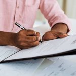 Closeup shot of an unrecognisable businessman filling in paperwork in an office